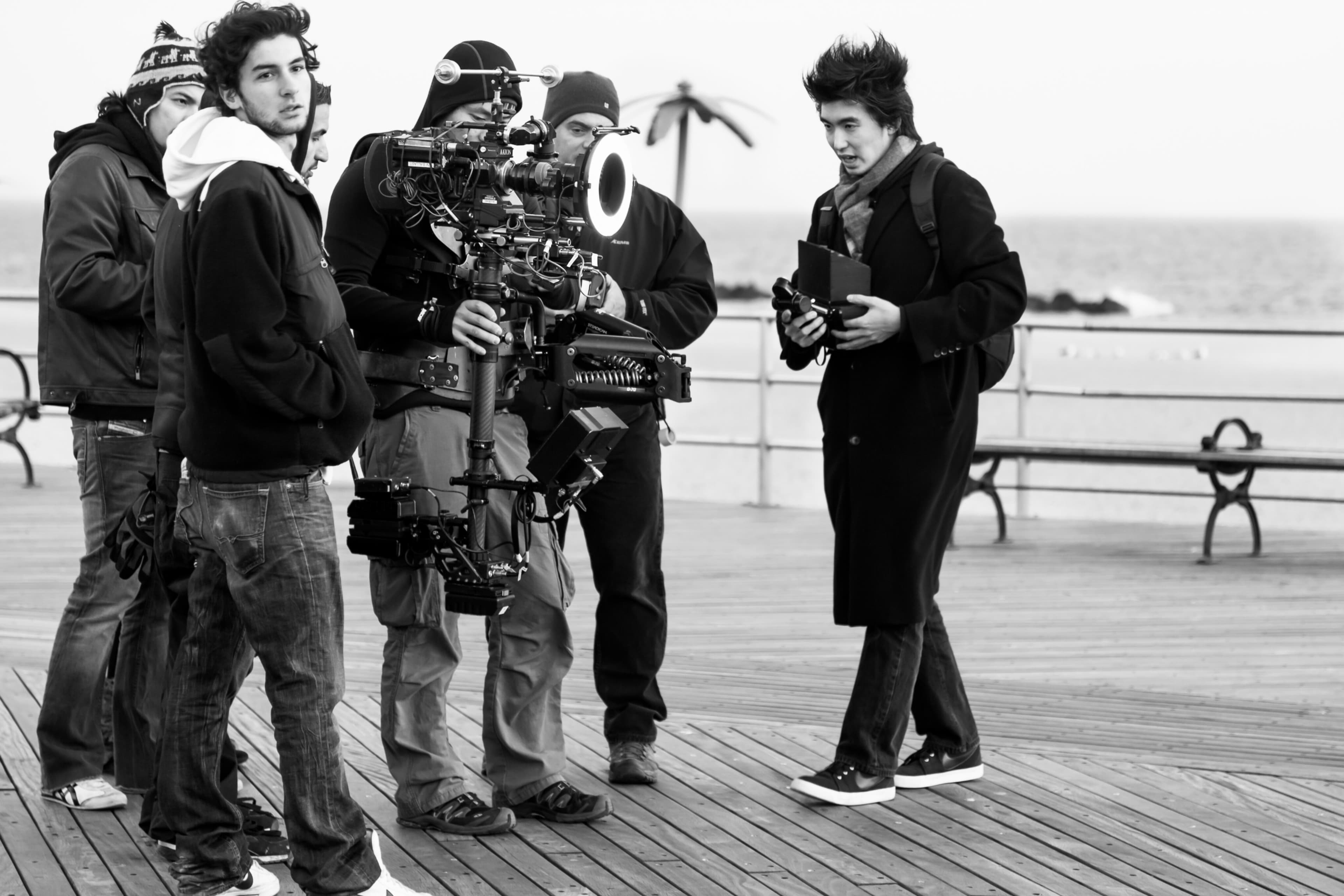 A group of people on a pier holding filming equipment and talking to each other